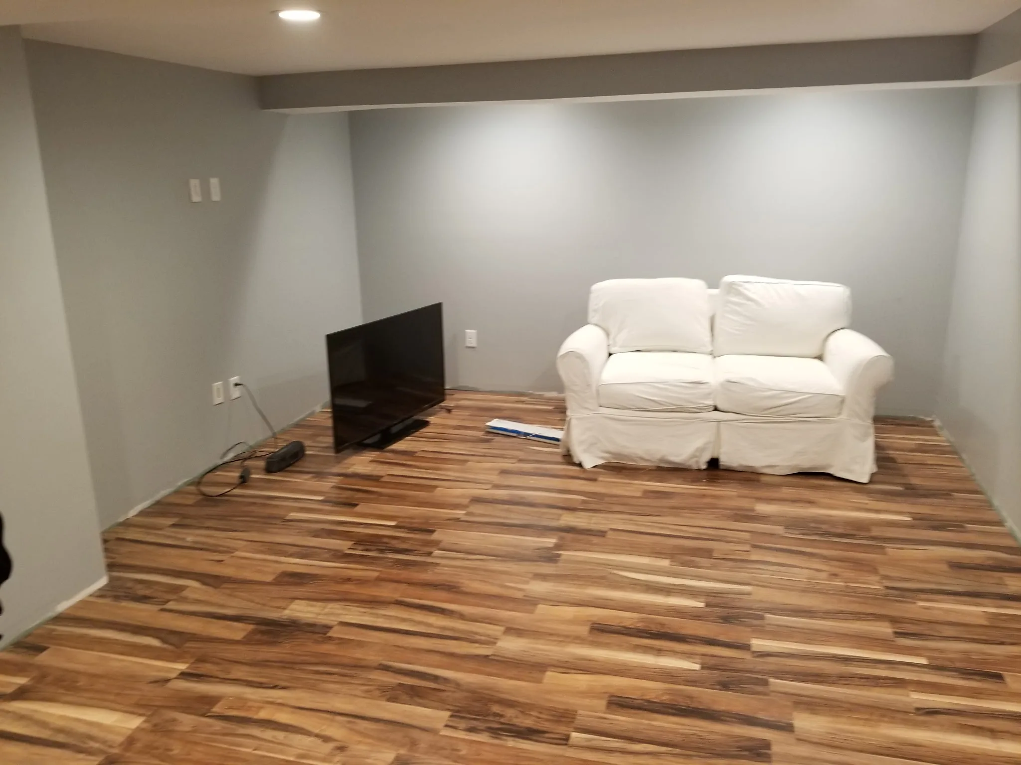 Finished basement family room with white loveseat and new wood-look flooring