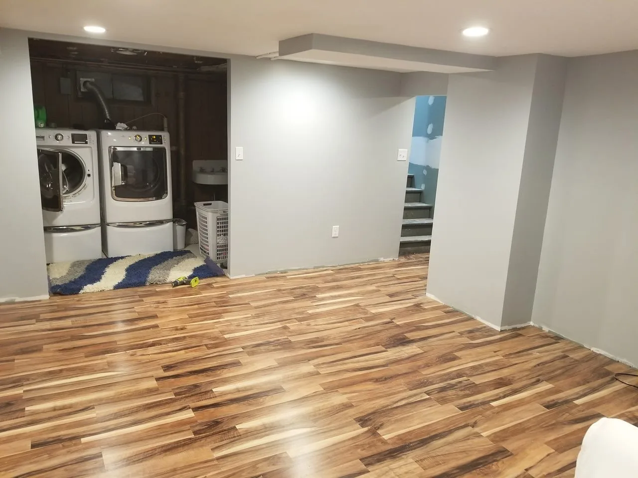 Finished basement with new wood-look flooring, recessed lighting, and laundry nook