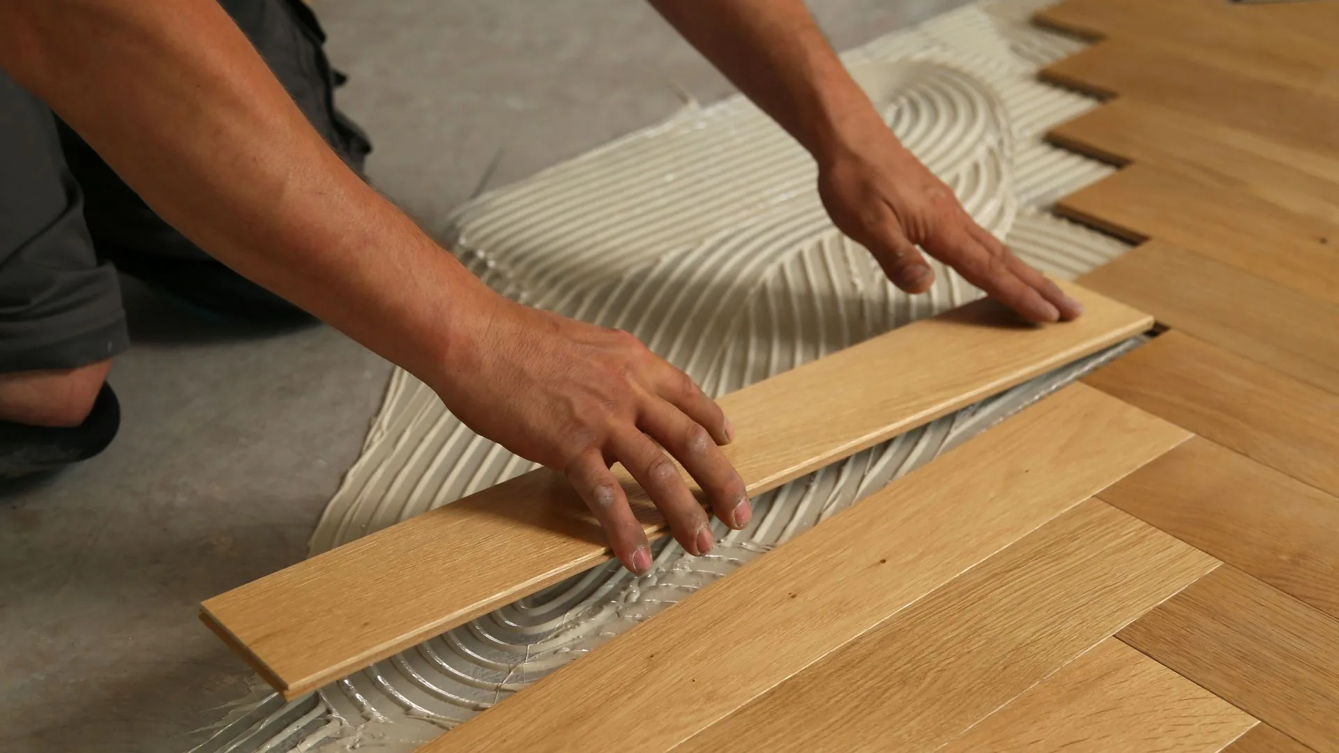 Installer laying herringbone plank flooring into adhesive
