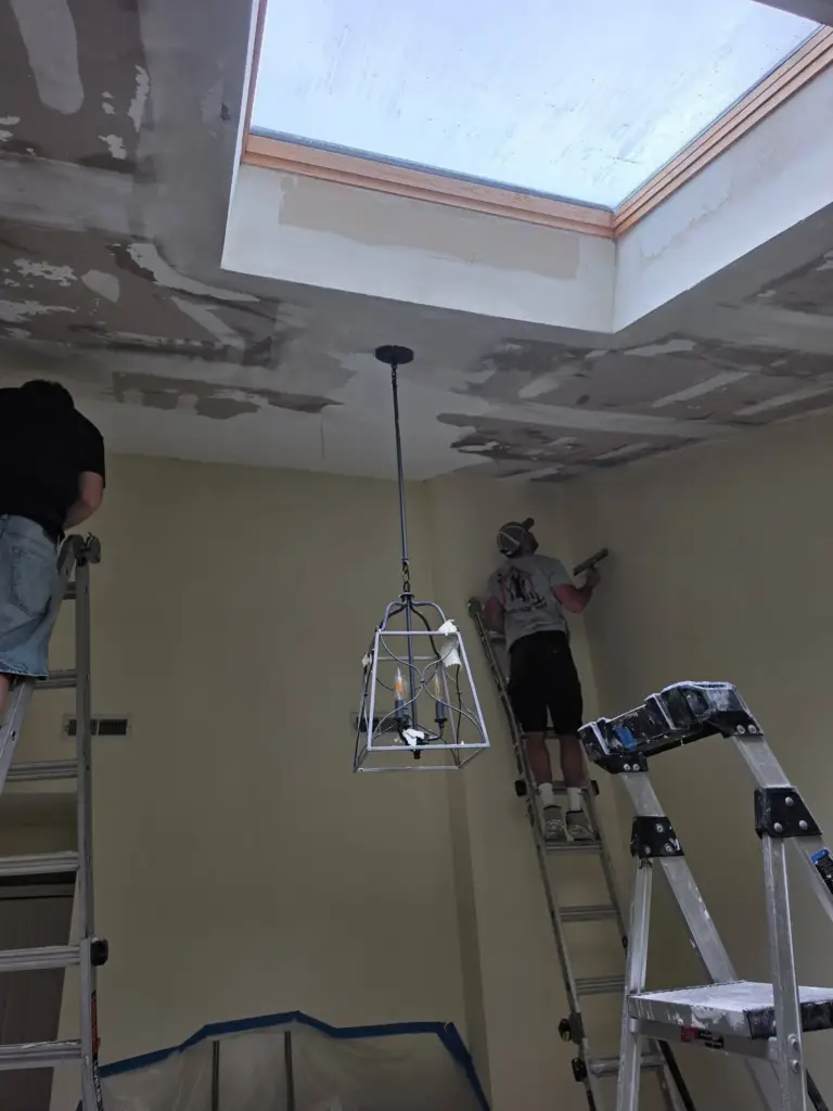 Two Myers Home Improvements crew members on extension ladders skim-coating a vaulted ceiling after popcorn texture removal