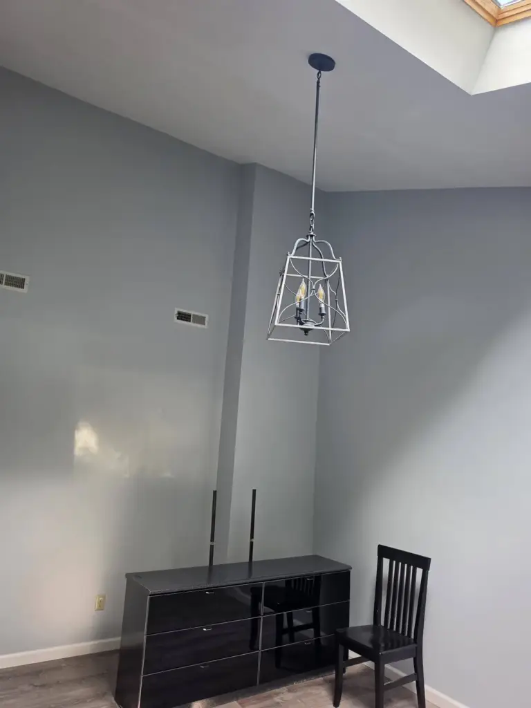 Tall vaulted wall painted soft gray-blue with white trim and a hanging lantern pendant after the remodel